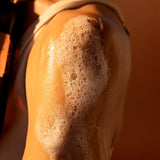 Close-up of a person's arm with soap suds on a warm-toned background