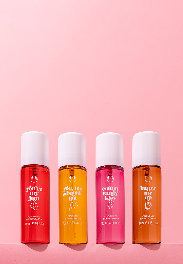 Four bottles of body spray with white caps on a pink background