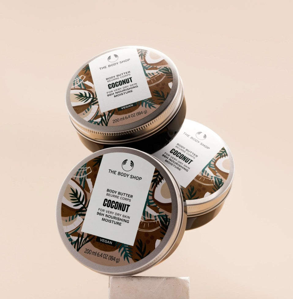 Three tins of The Body Shop Coconut body butter on a beige background