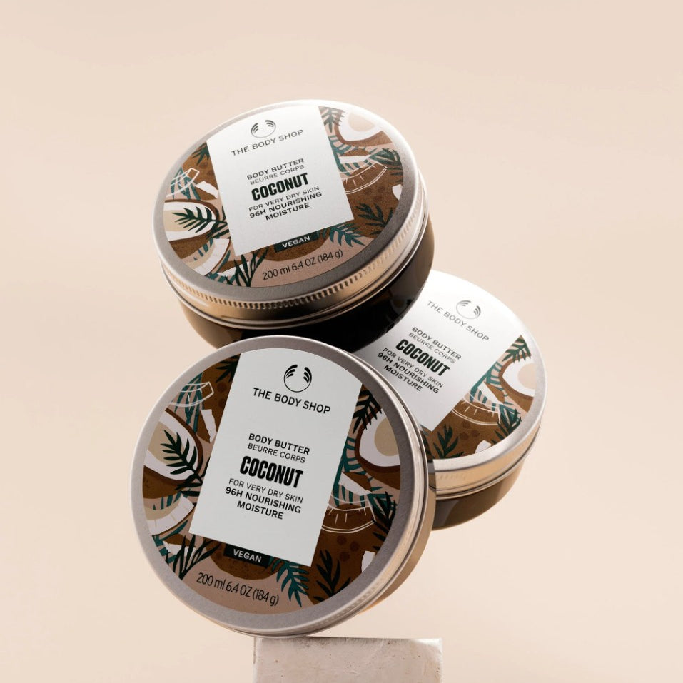 Three tins of The Body Shop Coconut body butter on a beige background