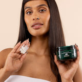 Woman holding a jar of body scrub and a bar of soap against a beige background