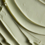 A close-up texture shot of a thick, creamy off-white cosmetic cream with smooth, swirled ridges.