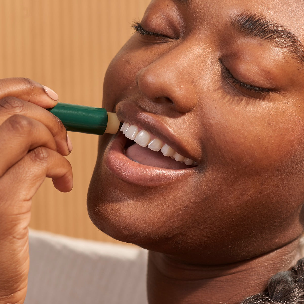 Person applying a green lip balm to their lips with a neutral background