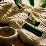 Two green containers and a small cup on a textured beige surface with leaves in the background.