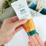 Hand holding a tube of The Body Shop Vitamin C product with a blurred background