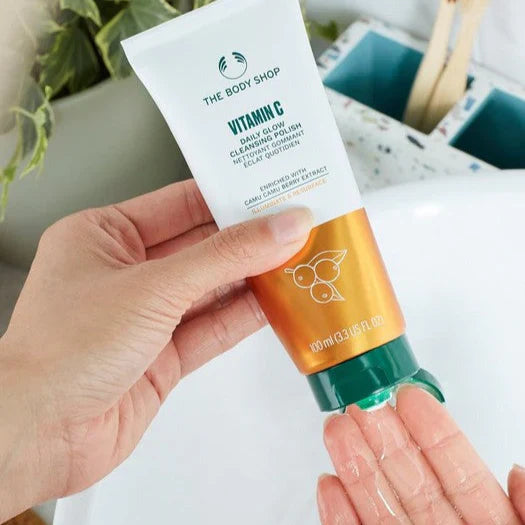 Hand holding a tube of The Body Shop Vitamin C product with a blurred background