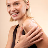 Woman applying cream to her shoulder against a beige background