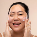 Woman applying cream to her face against a beige background