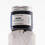 Jar of The Body Shop Charcoal Pore-Minimising Mask on a textured white background
