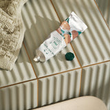 Hand cream tube on a tiled bathroom floor with a towel nearby