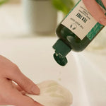 Person applying a green bottle of soap to a white cloth on a blurred background
