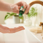 Person applying a green essential oil dropper to their palm with a blurred background