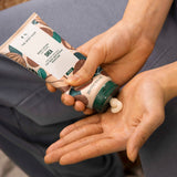 Person applying shea butter from a container to their hand, with a product packaging in the foreground.