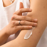 Hand applying cream to a person's arm with a neutral background