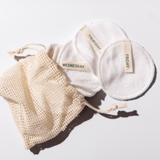 Set of reusable cotton pads with labels and a mesh storage bag on a light background