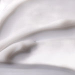 A close-up of a thick, creamy white cosmetic or skincare product with smooth, flowing texture and soft shadows.