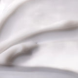 A close-up of a thick, creamy white cosmetic or skincare product with smooth, flowing texture and soft shadows.