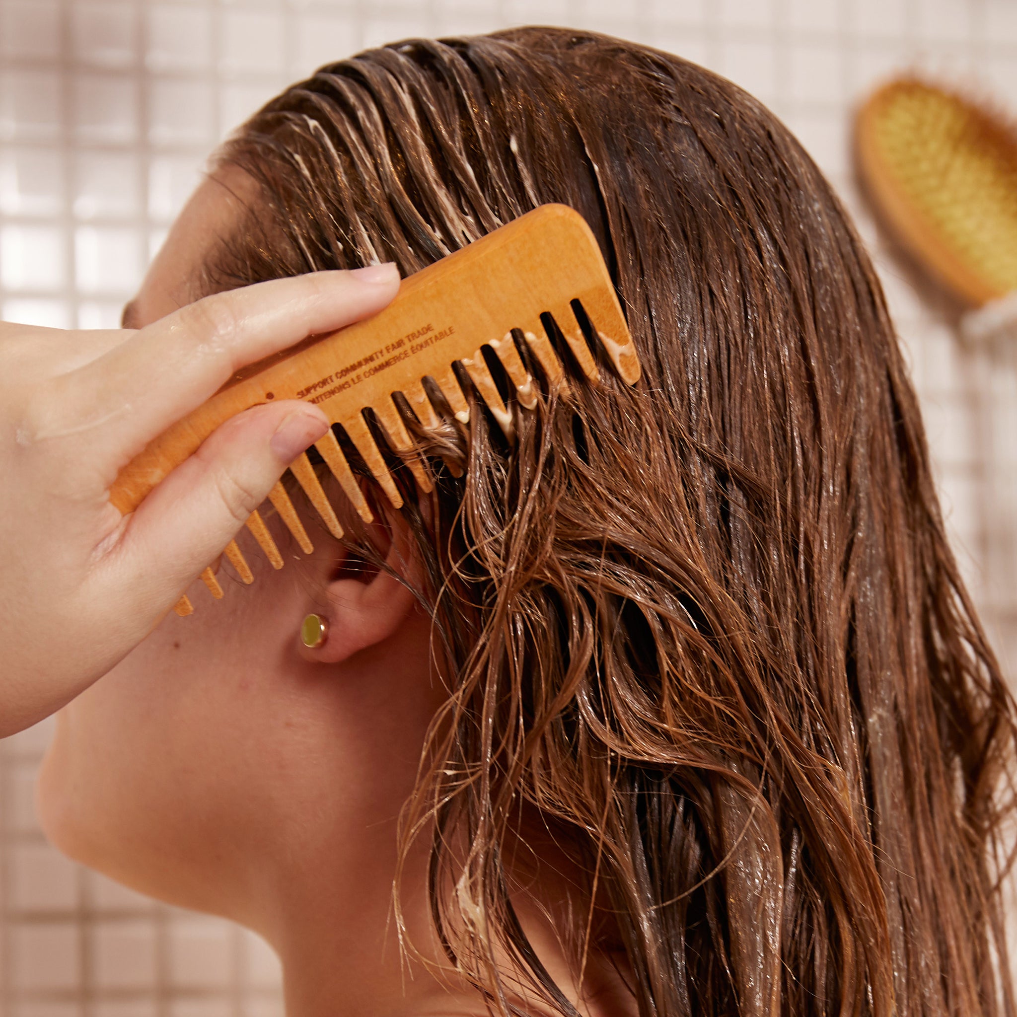 Person combing wet hair with a wooden comb in a bathroom setting
