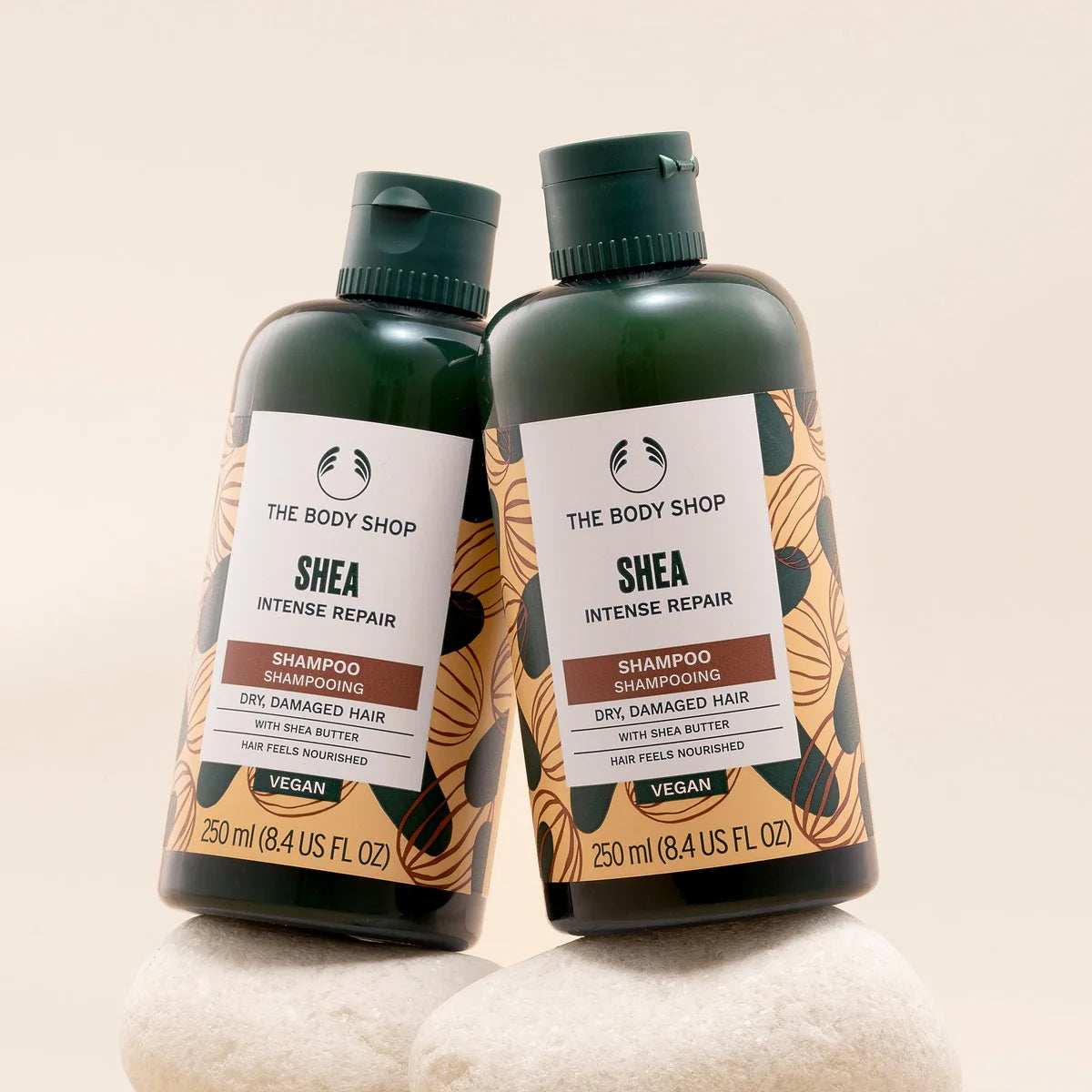 Two bottles of The Body Shop Shea Intense Repair Shampoo on a beige background