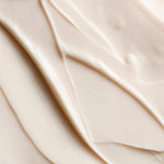 A close-up texture shot of a thick, creamy off-white cosmetic cream with smooth, flowing swirled lines.