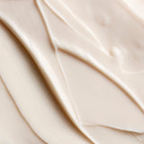 A close-up texture shot of a thick, creamy off-white cosmetic cream with smooth, flowing swirled lines.