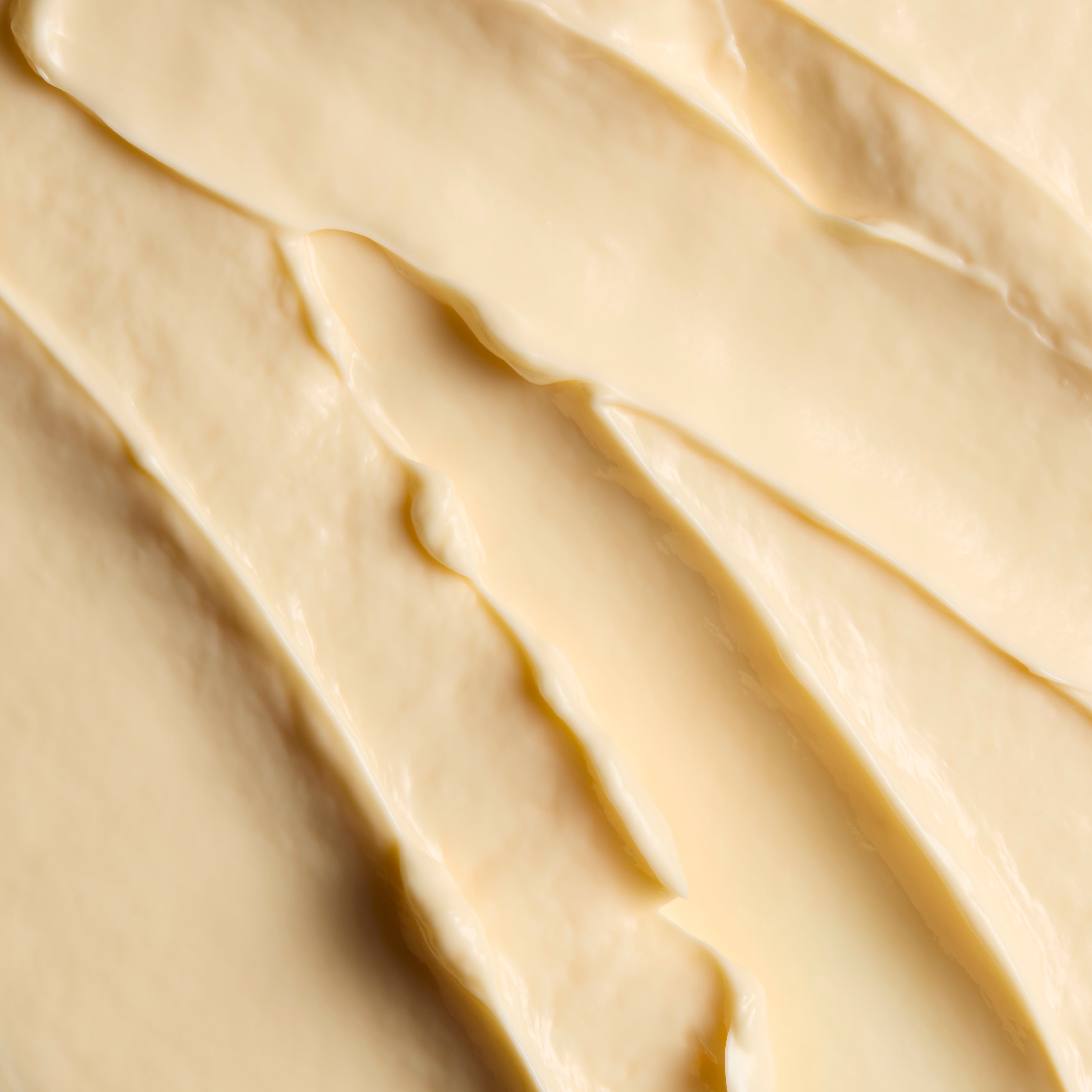 A close-up texture shot of a thick, creamy off-white cosmetic or food product with smooth diagonal swirled strokes.