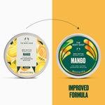 Two round tubs of The Body Shop Mango Body Butter are shown side by side on a split white and mustard yellow background, with a dotted arrow above indicating an improved formula. The left tub has a white lid with yellow citrus illustrations, and the right tub has a dark green lid with orange and yellow abstract leaf-like graphics.
