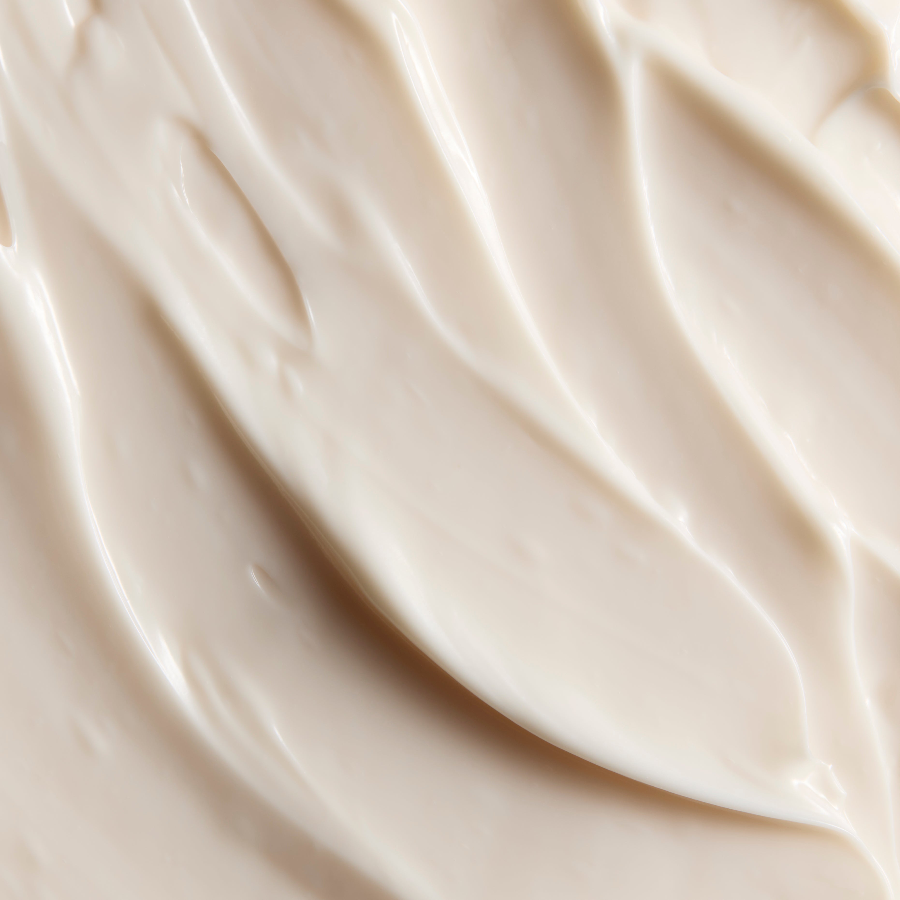 A close-up texture shot of thick, creamy off-white cosmetic cream with smooth, swirled ridges.
