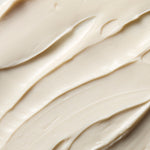 A close-up texture shot of a thick, creamy off-white cosmetic cream with smooth, swirled strokes.