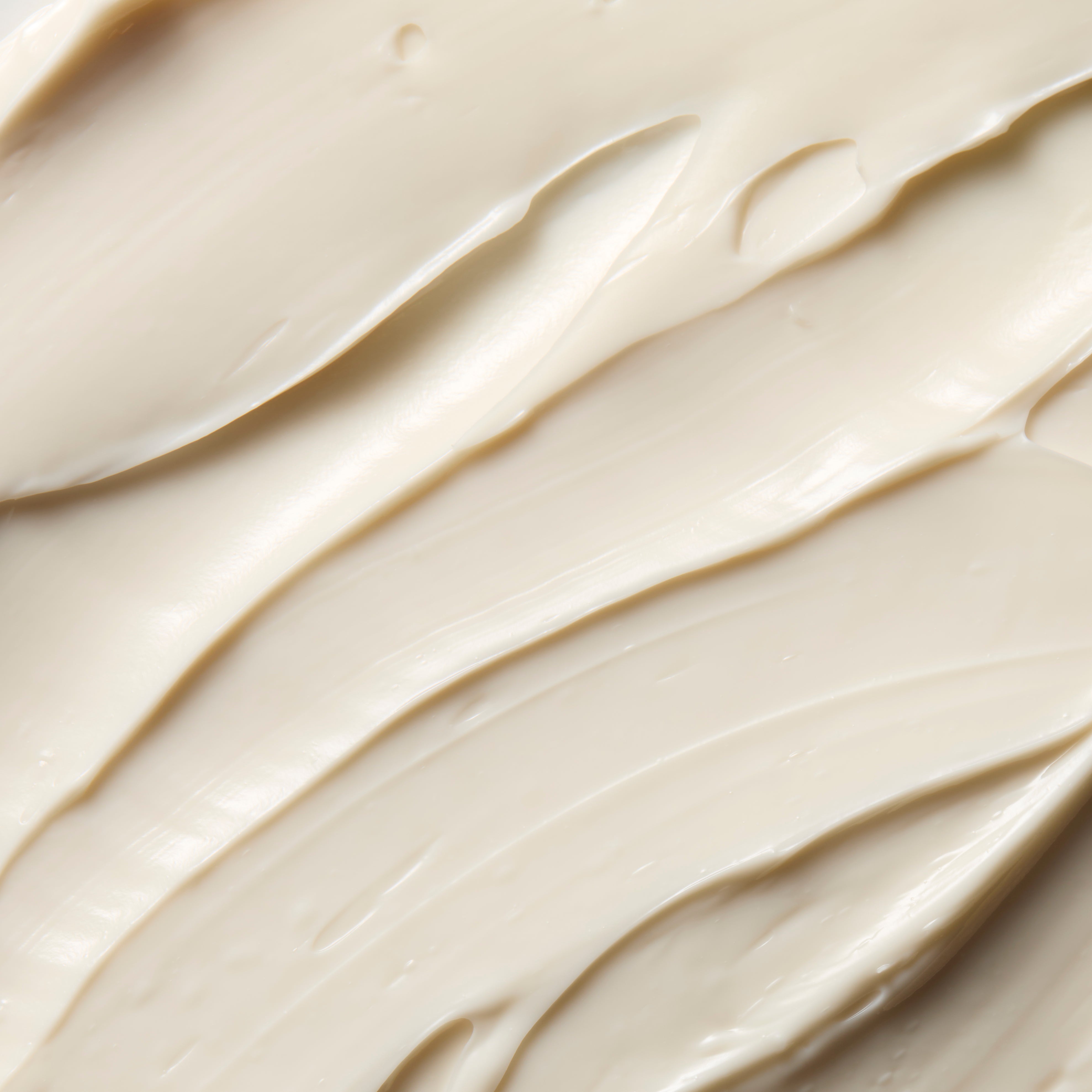 A close-up texture shot of a thick, creamy off-white cosmetic cream with smooth, swirled strokes.