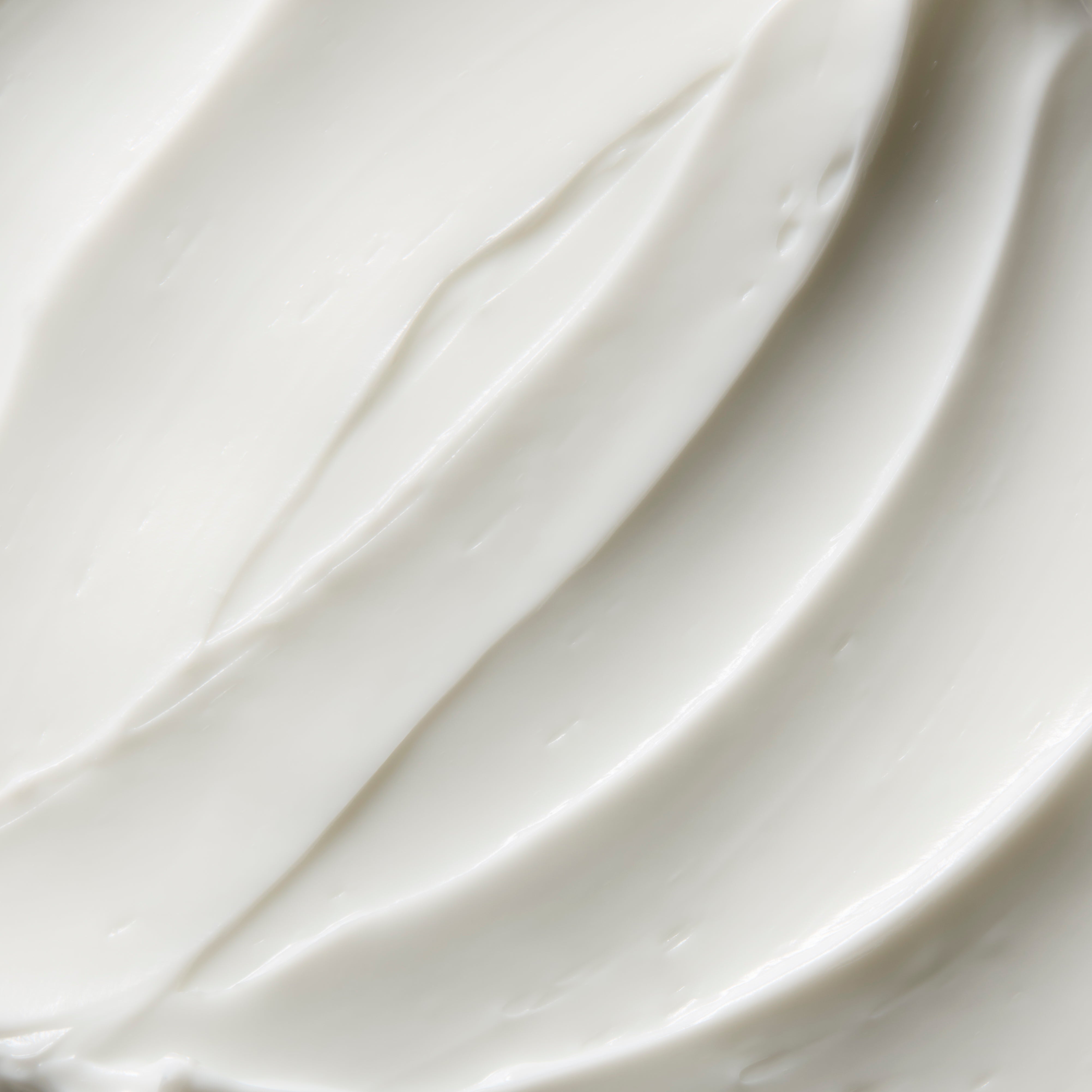 A close-up texture shot of thick, creamy white cosmetic cream with smooth, swirled strokes.