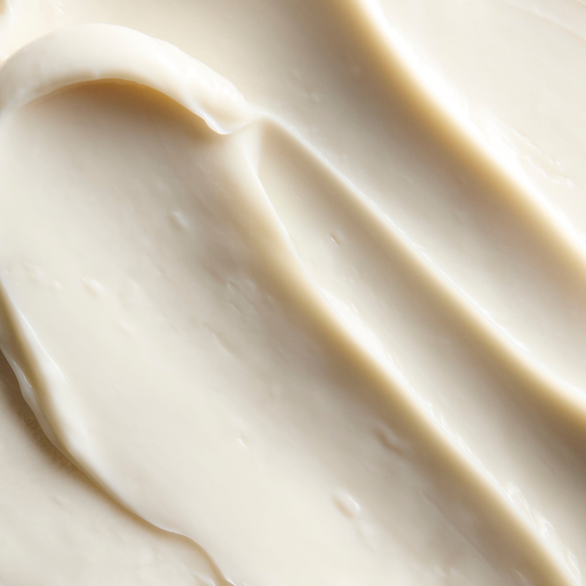 A close-up texture shot of a thick, creamy off-white cosmetic cream swirled on a matching background.