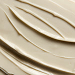 A close-up texture shot of a thick, creamy cosmetic cream or shampoo, swirled and spread with smooth, glossy ridges.