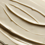 A close-up texture shot of a thick, creamy cosmetic cream or shampoo, swirled and spread with smooth, glossy ridges.