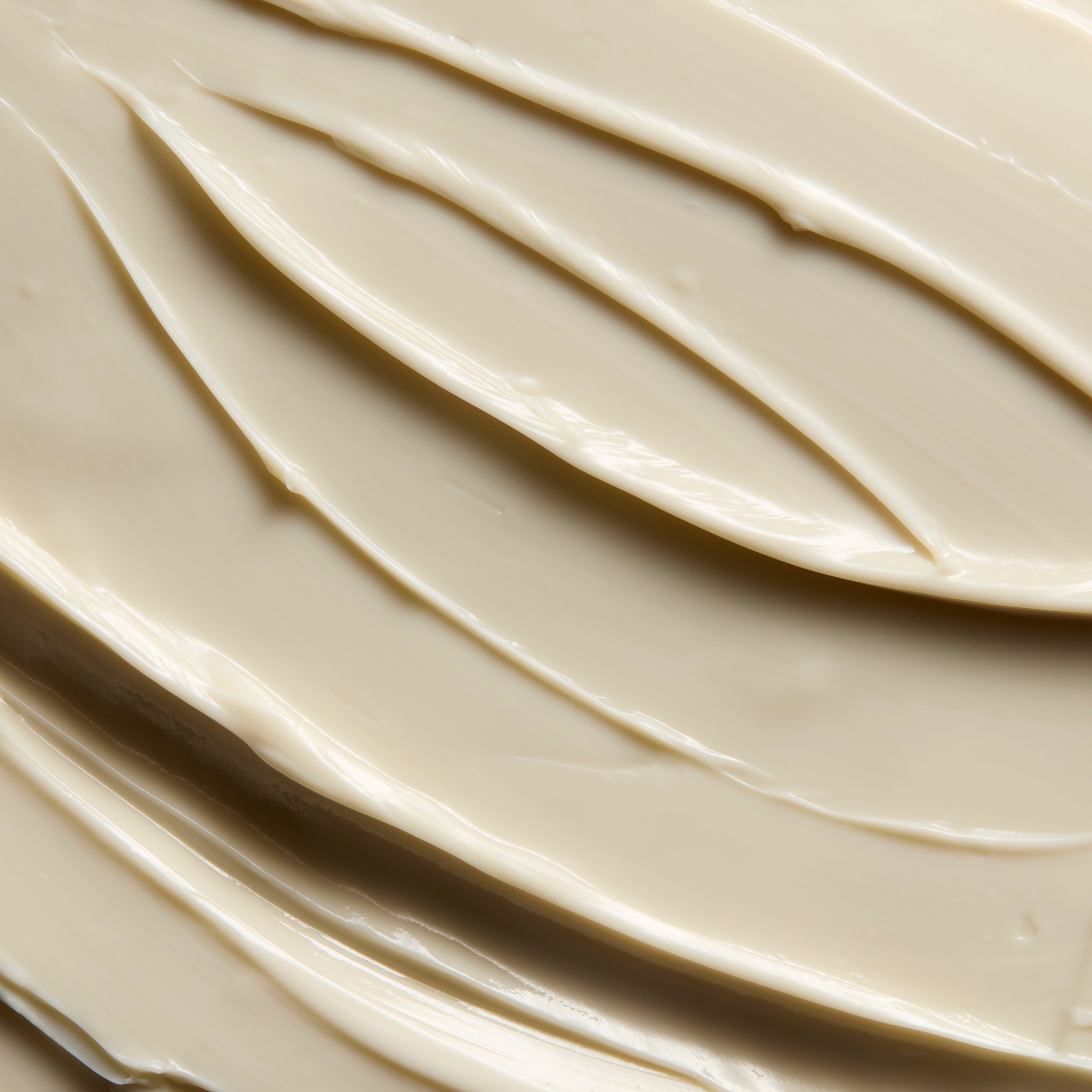 A close-up texture shot of a thick, creamy cosmetic cream or shampoo, swirled and spread with smooth, glossy ridges.
