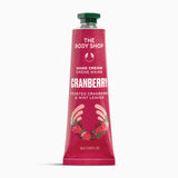 A squeeze tube of The Body Shop Hand Cream Creme Mains in Cranberry, featuring a deep pink-red tube with white text, a green cap, and illustrations of strawberries and hands at the bottom, set against a plain white background.