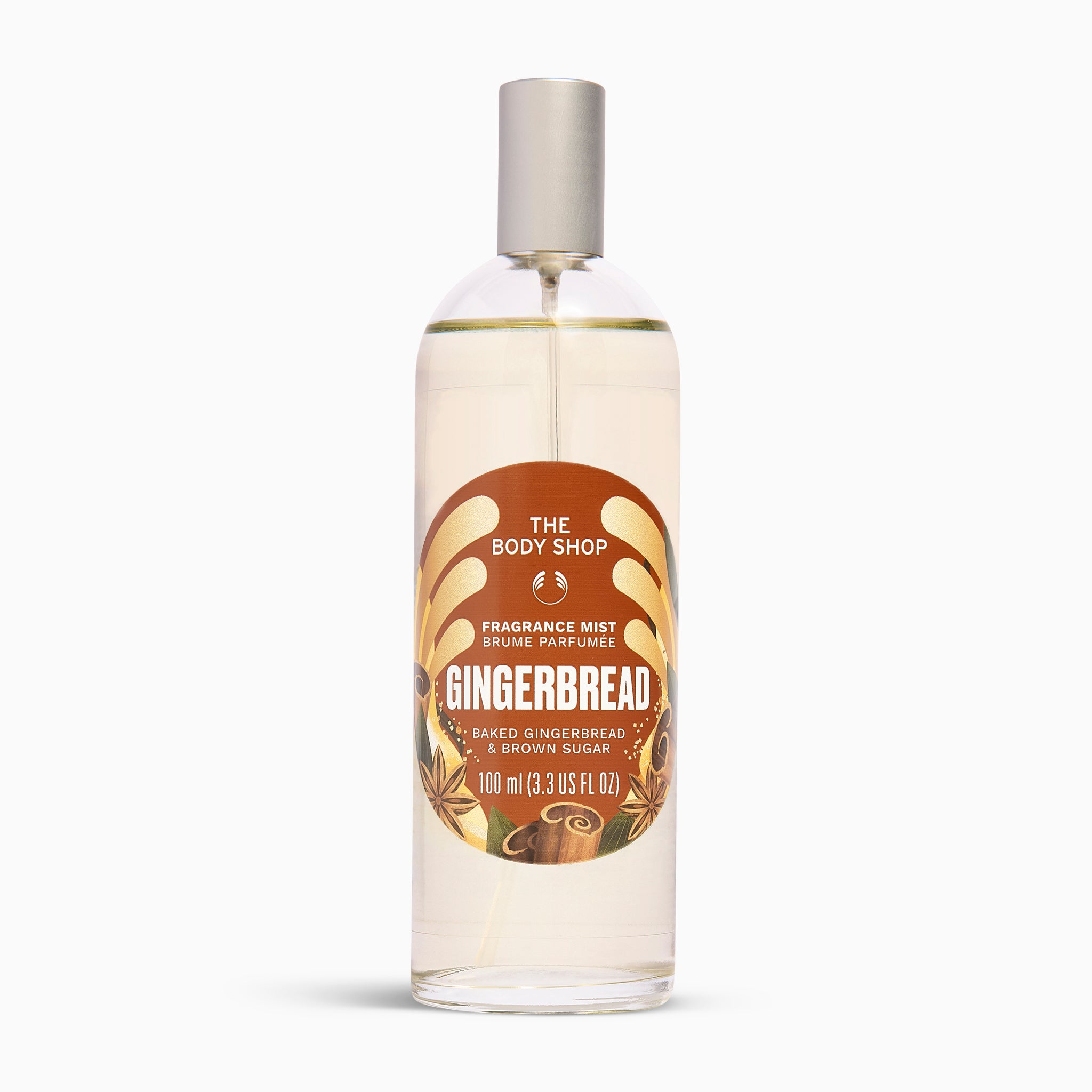 A clear glass bottle of The Body Shop Gingerbread Fragrance Mist with a silver spray cap and a brown and orange label, set against a plain white background.