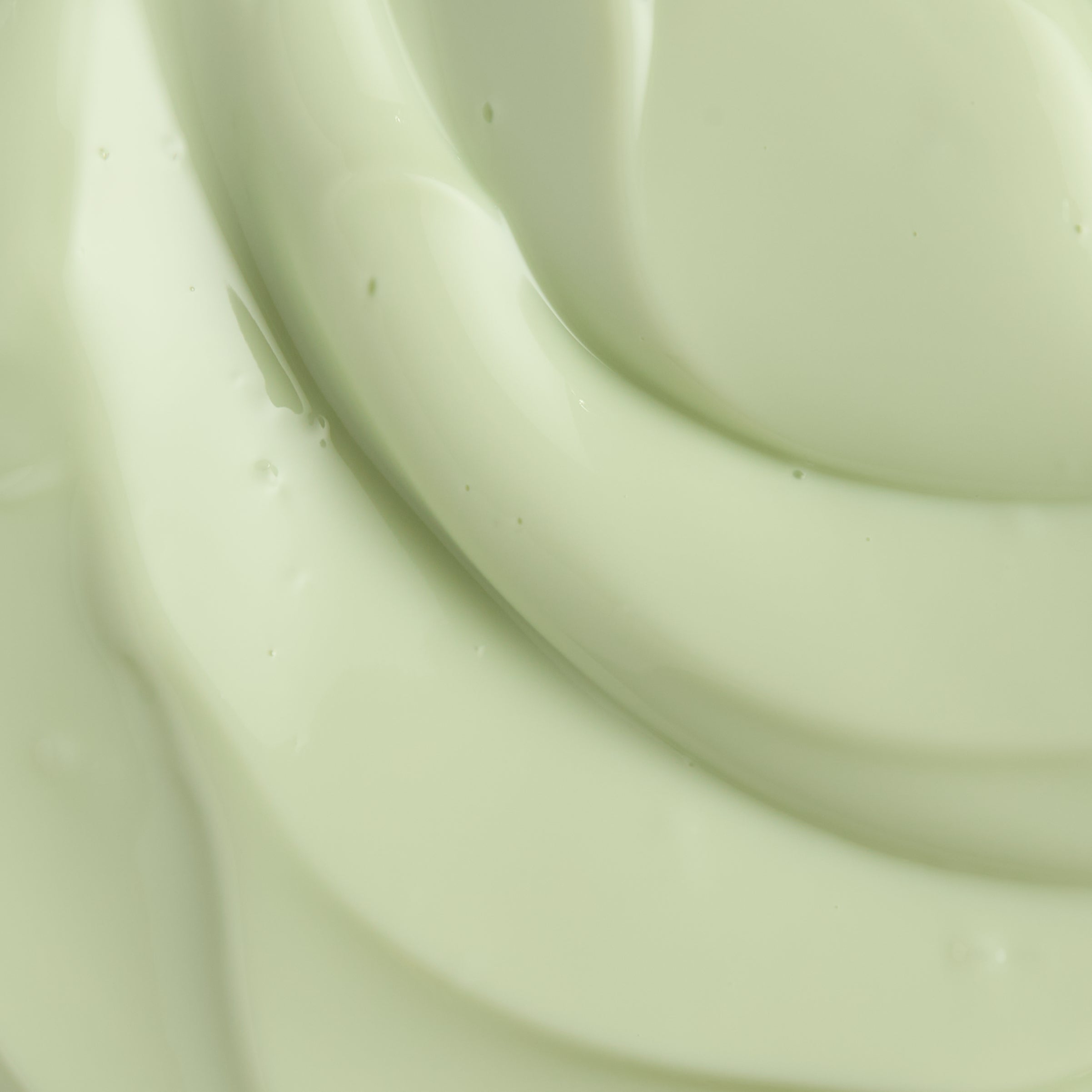 A close-up texture shot of a thick, creamy pale mint green cosmetic cream with smooth, glossy swirls.