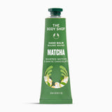 A squeeze tube of The Body Shop Hand Balm in Matcha flavor, featuring a green body with white text and illustrations of matcha leaves and chocolate pieces, set against a plain white background.