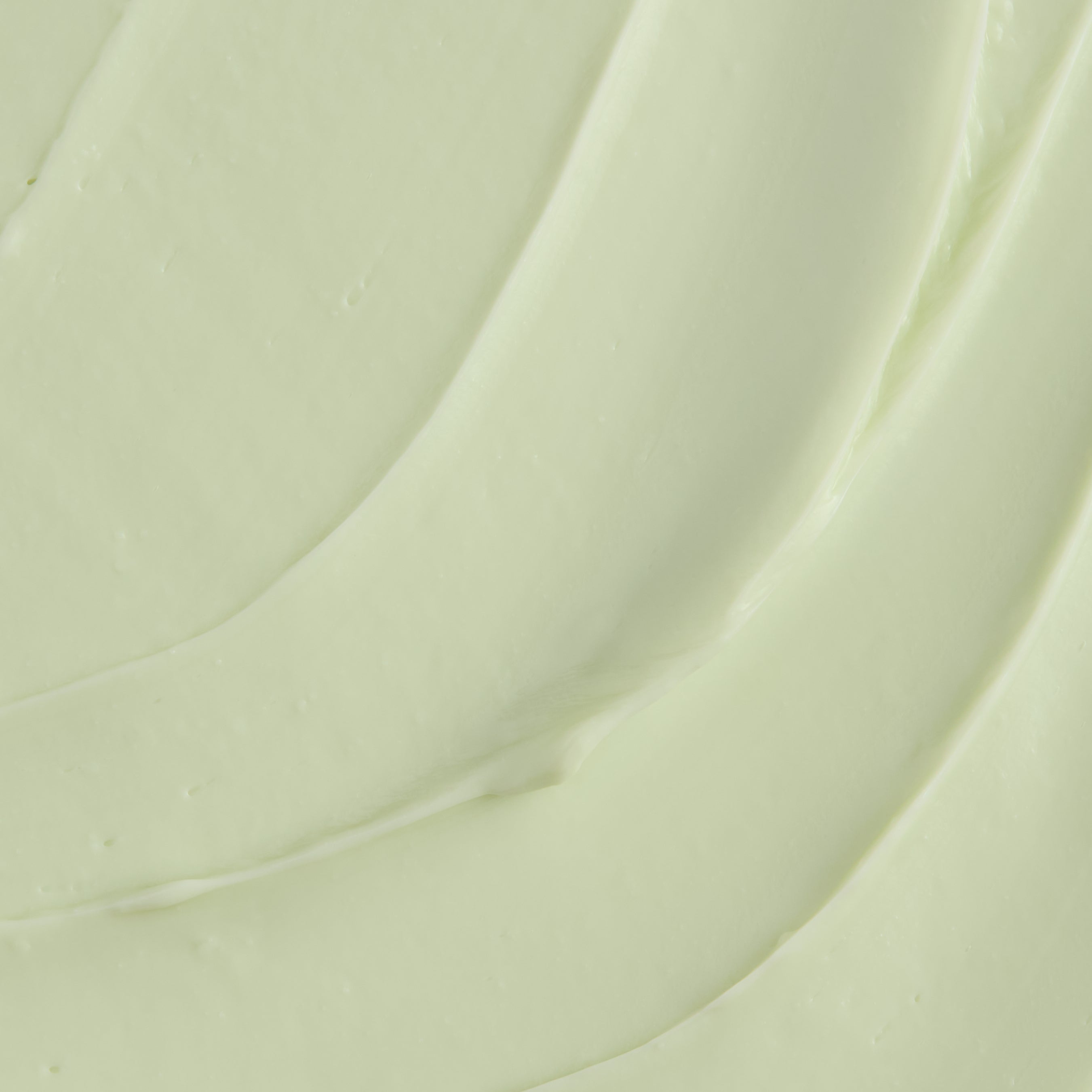A close-up texture shot of a thick, creamy pale green cosmetic cream with smooth, flowing swirled lines.