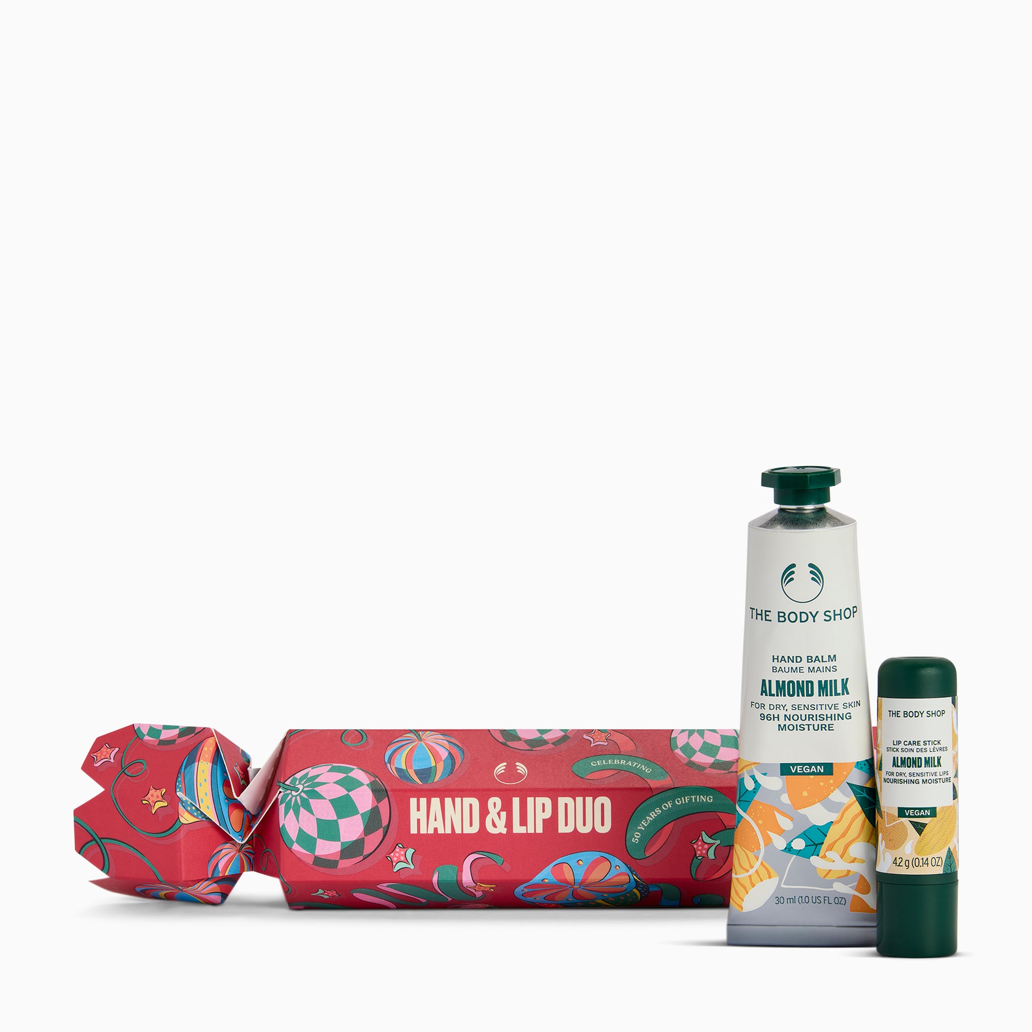 The Body Shop Hand & Lip Duo gift set featuring a red patterned cracker-style gift box, a tube of Hand Balm in Almond Milk, and a lip balm stick, arranged on a clean white background.