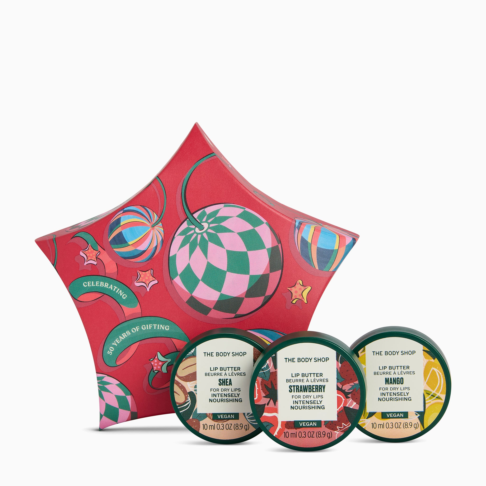 The Body Shop Christmas gift set featuring a red star-shaped box with colorful ornaments and three round lip balm tubs in front, labeled Shea, Strawberry, and Mango.
