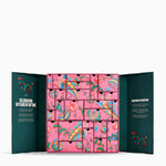 An open advent calendar with a pink front panel featuring many small illustrated drawers, flanked by dark teal inner flaps with decorative text and red botanical details, shown on a light gray background.