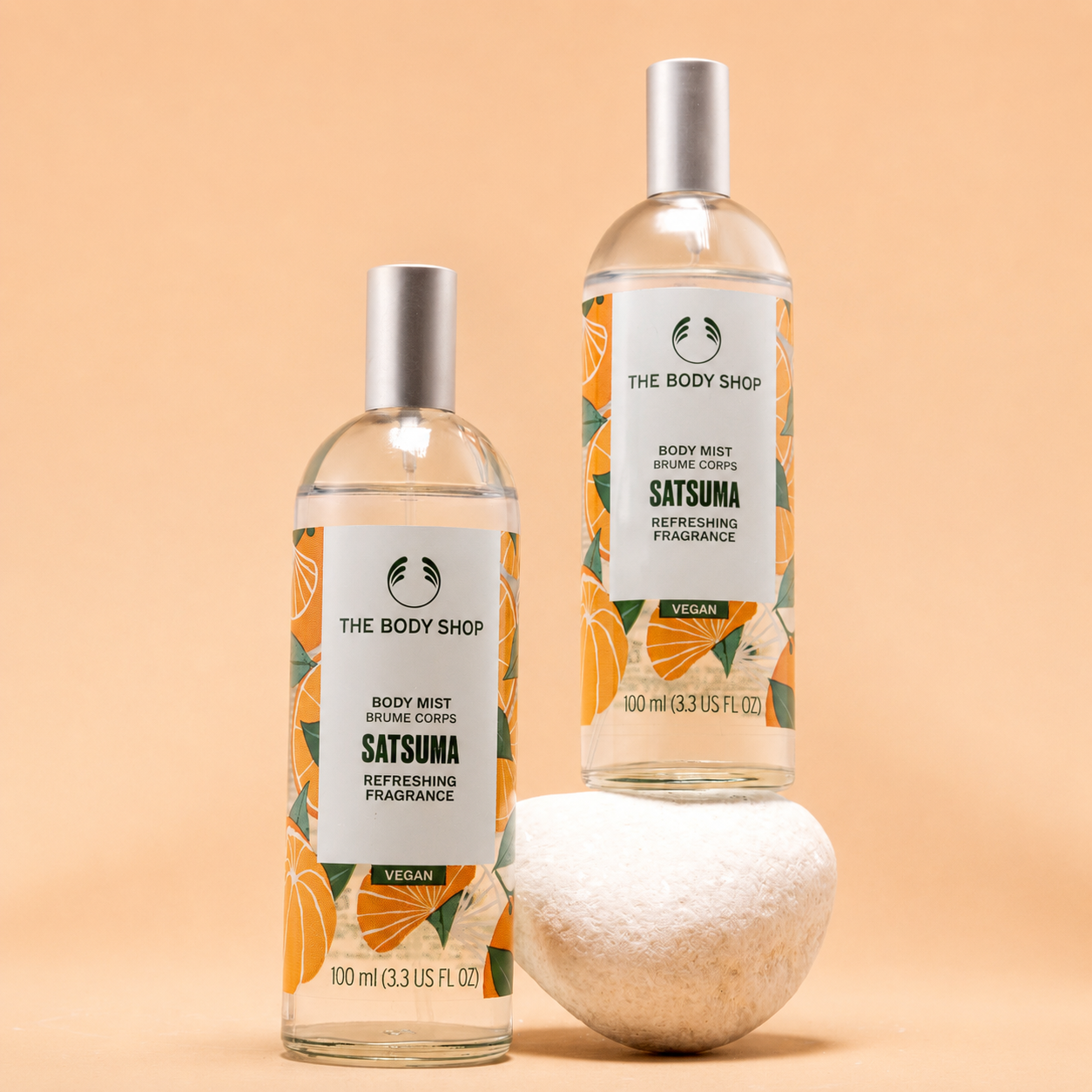 Two bottles of The Body Shop Satsuma body mist on a peach background
