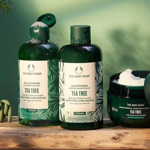 The Body Shop Tea Tree hair care products on a wooden surface with a green blurred background.