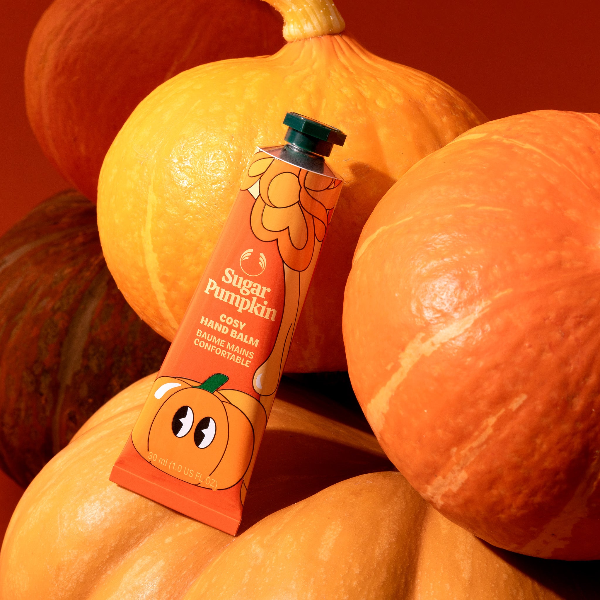 Hand balm with a pumpkin design surrounded by pumpkins on a warm-toned background