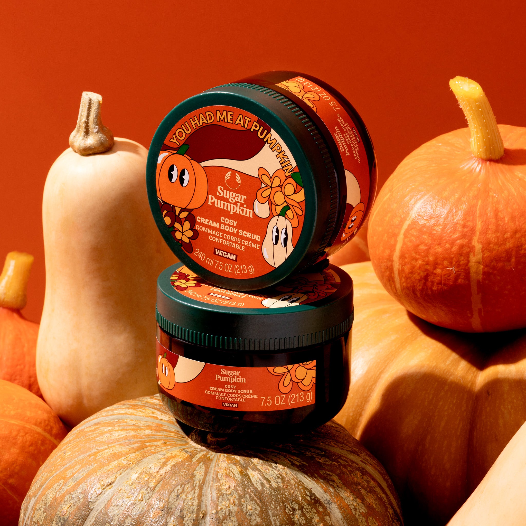 Two jars of 'Sugar Pumpkin Cream Body Scrub' on pumpkins with an orange background
