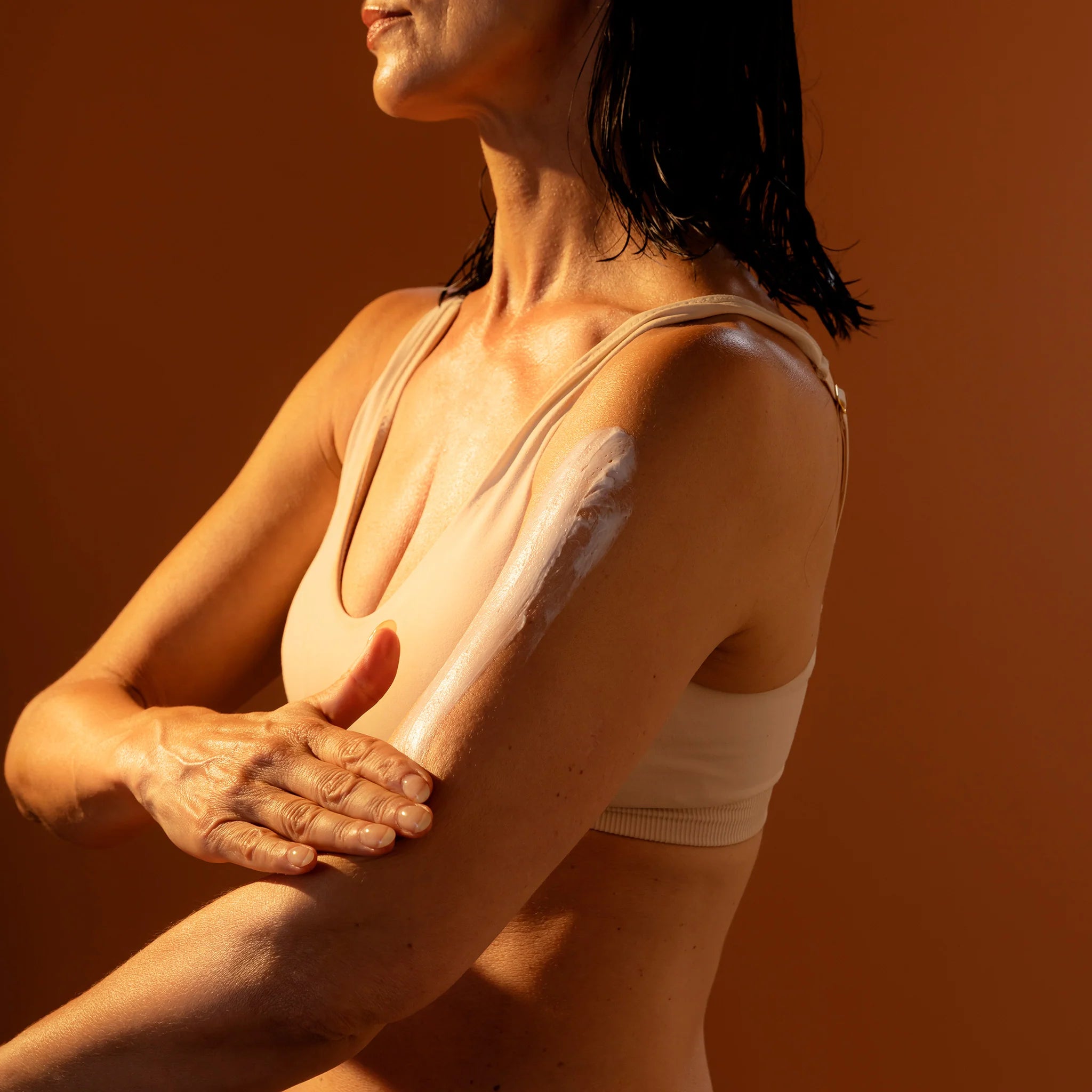 Woman with wet hair and arm lotion against a brown background