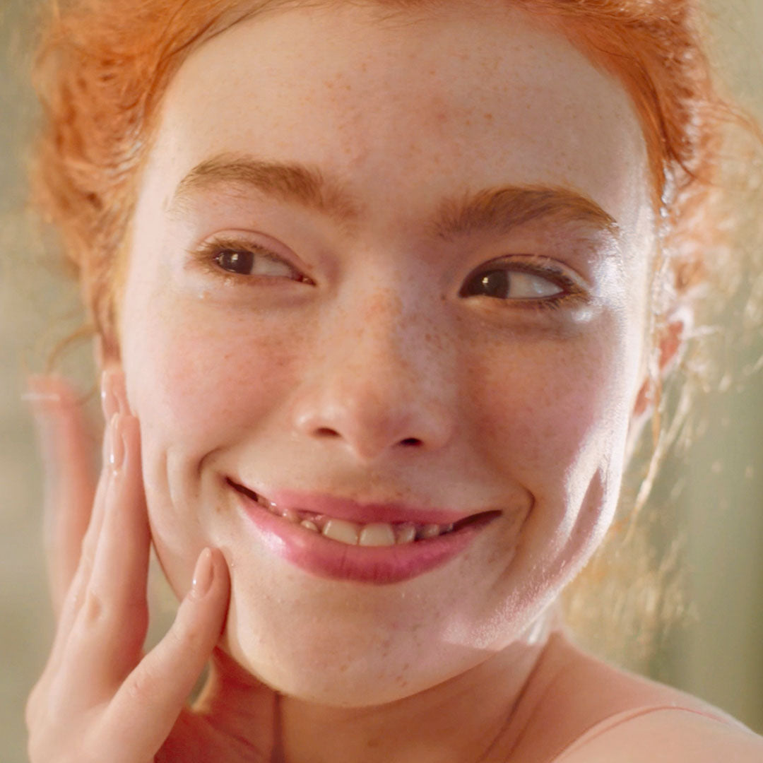 Close-up of a person with freckles and red hair, touching their face.
