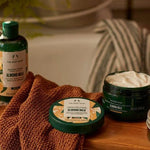 The Body Shop Almond Milk products on a wooden surface with a towel and bathtub in the background.